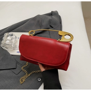 Detail of red rectangular clutch bag with golden safety pin handle and chain strap
