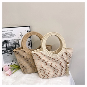 Detail of woven straw bucket bags in beige and khaki with ring handles and tassel charms