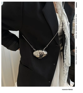 Detail of a mini silver metallic shell bag with a sleek mirror finish and chain strap