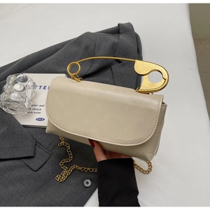 Close-up of cream square handbag with unique gold safety pin handle and chain strap