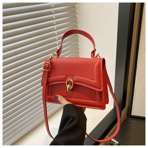 Detail of red minimalist crossbody bag with golden metal twist lock and sleek leather texture