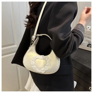 Close-up of cream heart lace crossbody bag worn by a model in a black blazer
