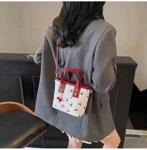 Detail of white leather cherry print bucket bag with red handles and matching charm