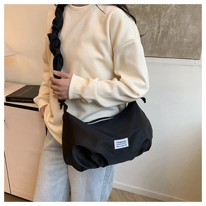Détail du sac croissant noir avec bandoulière plissée et étiquette tissée tendance