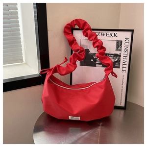 Détail d'un sac hobo rouge avec bandoulière froncée posé sur une table en métal argenté
