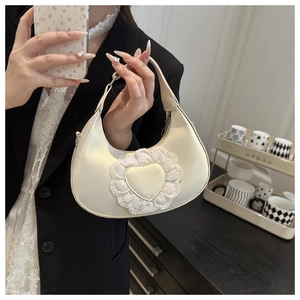 Detail of a beige crescent bag with heart lace trim held in a cozy home setting