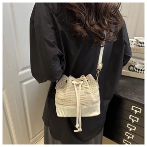 Detail of hand-woven straw bucket bag with white leather straps and gold buckle accents