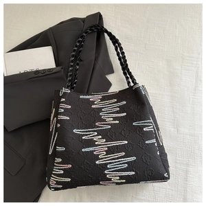 Close-up of black quilted tote bag featuring colorful wavy embroidery and braided handles