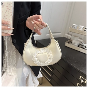 Detail of a cream crescent handbag with delicate lace heart applique and top handle