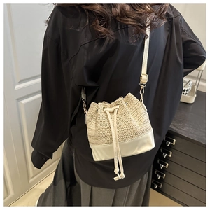 Detail of beige straw drawstring bucket bag with white leather base and shoulder strap