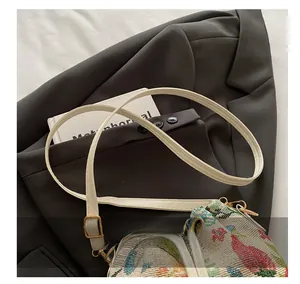 Close-up of white leather shoulder strap with gold buckle and jacquard bucket bag detail