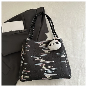 Detail of black quilted tote bag featuring colorful embroidery and panda plush charm