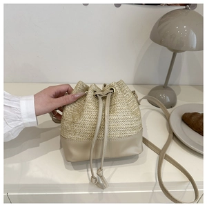 Detail of beige straw bucket bag with leather base and drawstring on white table