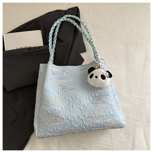 Detail of light blue textured tote bag with woven handle and a cute panda plush charm