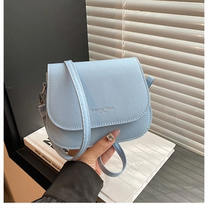 Detail of light blue crossbody saddle bag with silver metal hooks and fashion text