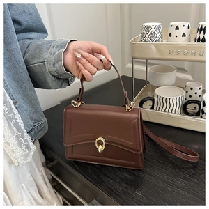 Brown PU crossbody bag with elegant gold twist lock and dual strap on a desk