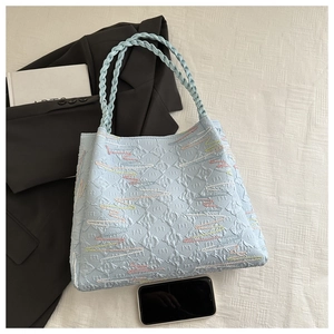 Top view of large light blue tote bag with monogram texture and woven handles on a suit