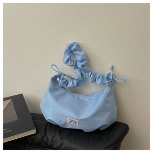 Détail d'un sac croissant bleu clair avec bandoulière plissée et étiquette mode