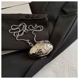 Close-up of a silver shell-shaped mini bag with a sleek snake chain on a black blazer
