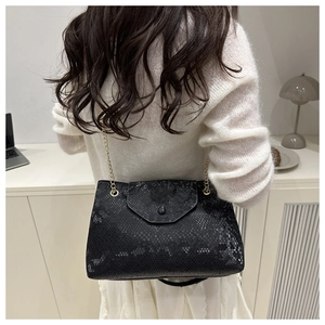 Détail du sac bandoulière noir imprimé serpent avec chaîne dorée porté par un mannequin