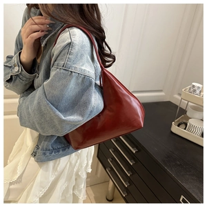 Close-up of stylish burgundy patent leather shoulder bag worn on shoulder by a model