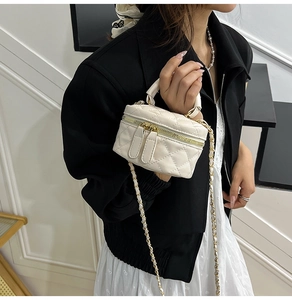 Close-up of cream quilted mini chain bag with gold metal zipper and leather handle
