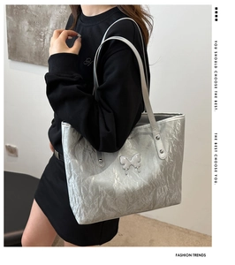 Detailed view of silver tote bag with crinkled texture and metal butterfly emblem