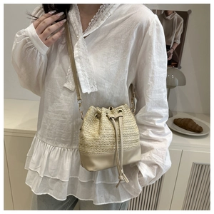 Detail of straw and leather bucket bag featuring a drawstring closure and slim shoulder strap