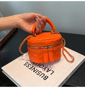 Detail view of bright orange quilted mini key bag with double zippers and chain strap