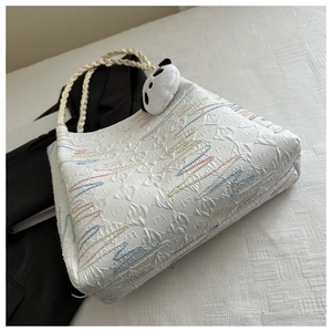 Detail of white textured tote with wave embroidery and woven rope handle and panda charm