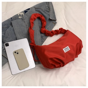 Détail d'un sac cabas plissé rouge avec bandoulière froncée et étiquette mode sur un lit