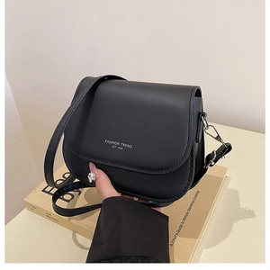 Detail of matte black crossbody bag with white fashion trend text and silver hardware