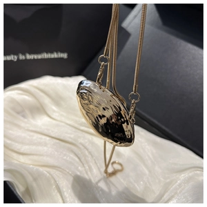 Macro detail of golden seashell-shaped mini bag pendant with hammered metal texture