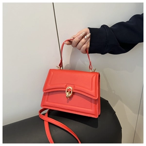 Detail of red leather crossbody bag featuring gold double ring buckle and textured stitching