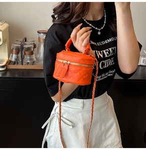 Close-up of orange quilted mini bag with gold zippers and chain strap detail