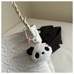 Cute plush panda charm with pink flower detail hanging on a textured white leather bucket bag