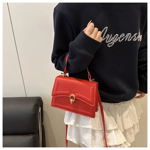 Detail of red crossbody bag with golden ring buckle shown on a model outfit