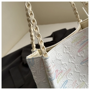 Detailed shot of beige bucket bag featuring colorful embroidery and woven handle