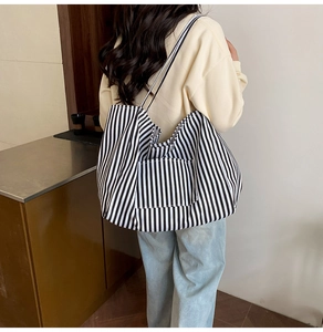 Close-up of a large black and white striped canvas tote bag worn on a woman's shoulder