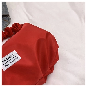Détail d'un sac à bandoulière en nylon rouge avec poignée froncée et étiquette
