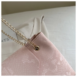 Détail du sac bandoulière rose à texture serpent avec bandoulière chaîne dorée