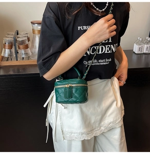 Model trägt eine dunkelgrüne gesteppte Mini-Zylindertasche mit goldener Kette