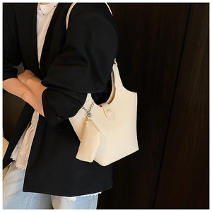 Detail of cream white bucket bag with pebble leather texture and mini charm on a model