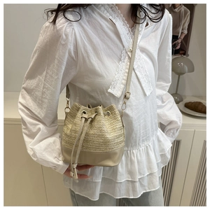 Detail of woven straw bucket bag with beige leather trim and drawstring closure