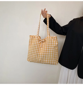 Close-up of yellow plaid canvas tote bag with a decorative bow detail and woven texture