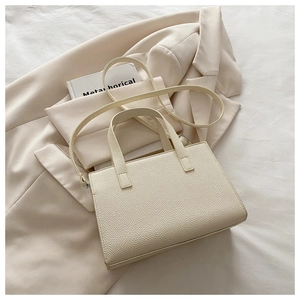 Close-up of cream lychee texture leather handbag on a beige suit, detail of grain and strap
