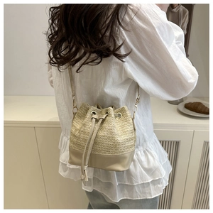 Detail of cream straw bucket bag with leather drawstring and metallic eyelets on model
