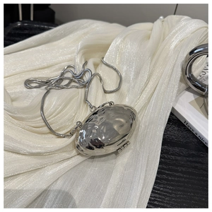 Détail d'un mini sac argenté en forme de coquillage avec texture ondulée et chaîne fine