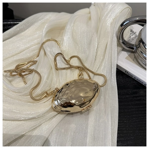 Detailed close-up of a gold shell-shaped metal clutch with a sleek snake chain strap