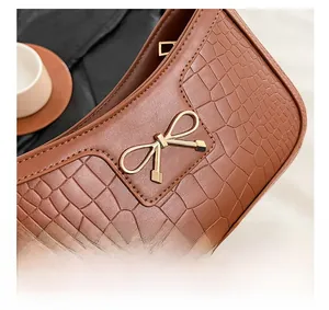 Detail shot of brown crocodile embossed leather bag with gold bow clasp